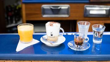 Una barra con diferentes bebidas, incluyendo un vaso de zumo de naranja, un capuchino y dos chupitos.