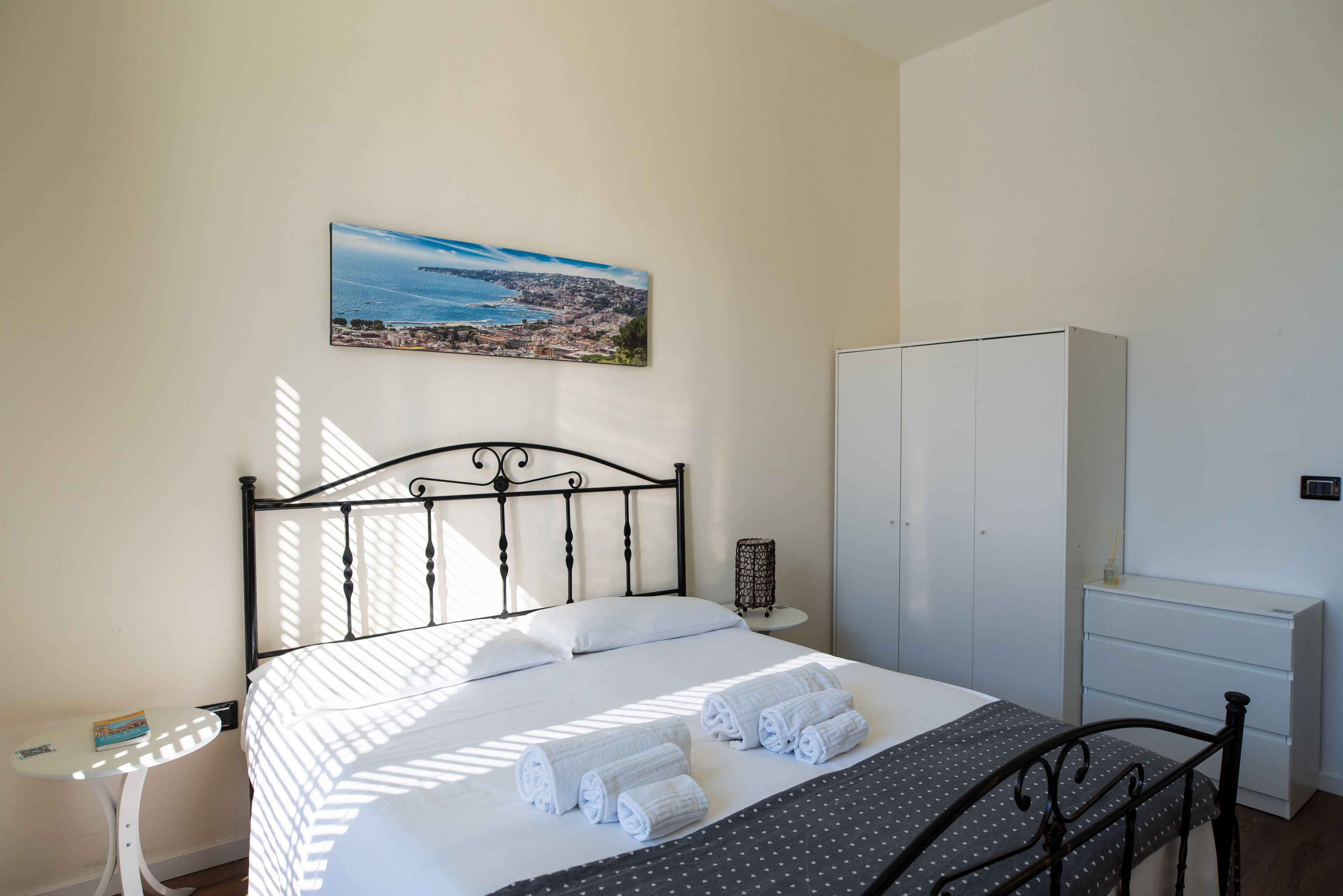 Een keurig opgemaakt slaapkamer met een bed, een nachtkastje, een kledingkast en een schilderij aan de muur.