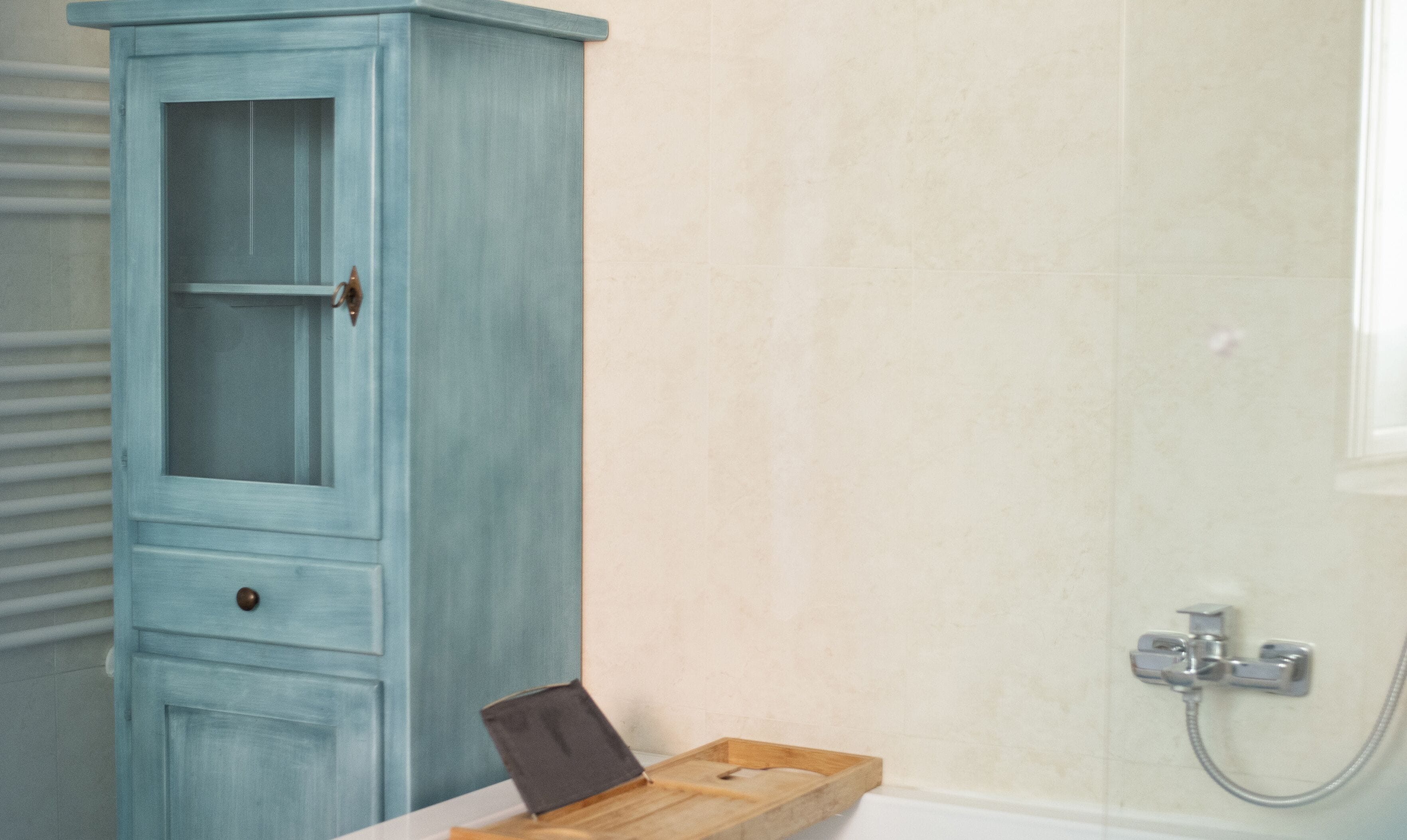 A bathroom with a light blue cabinet, a wooden tray, and a shower area.