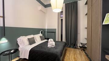 A hotel room with a bed, a bedside table, a lamp, and a view of the outside.