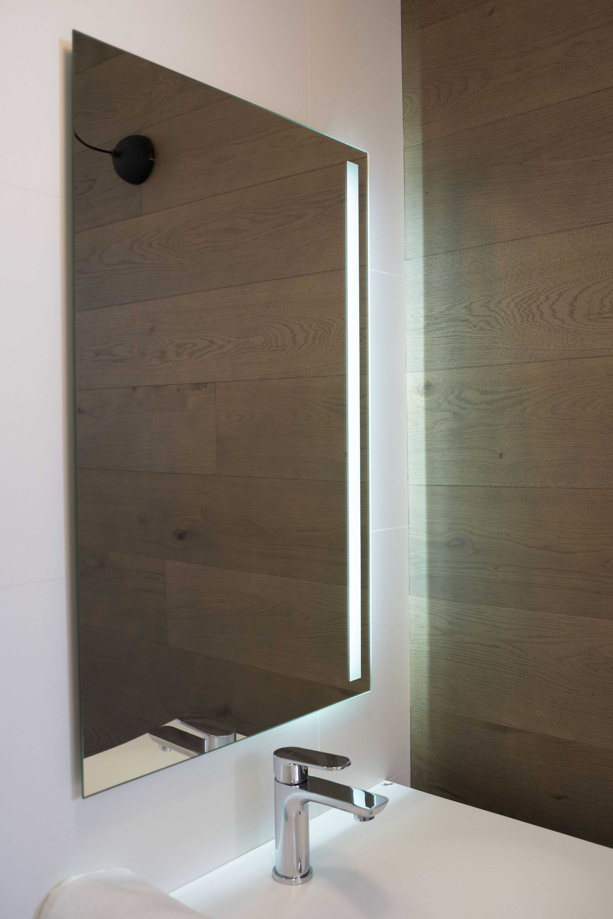 A bathroom with a modern design, featuring a large mirror, a chrome faucet, and wooden flooring.