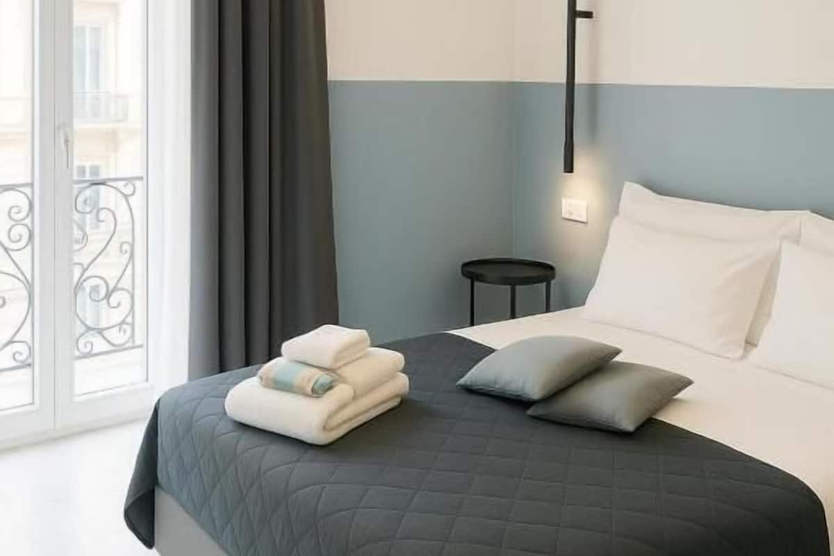Une chambre à coucher moderne avec un lit, une table de chevet, une lampe et une vue sur l’extérieur.