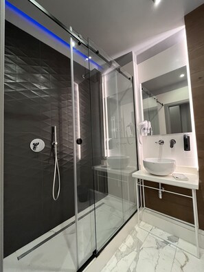 A modern bathroom with a glass-enclosed shower, a white sink, and a large mirror.