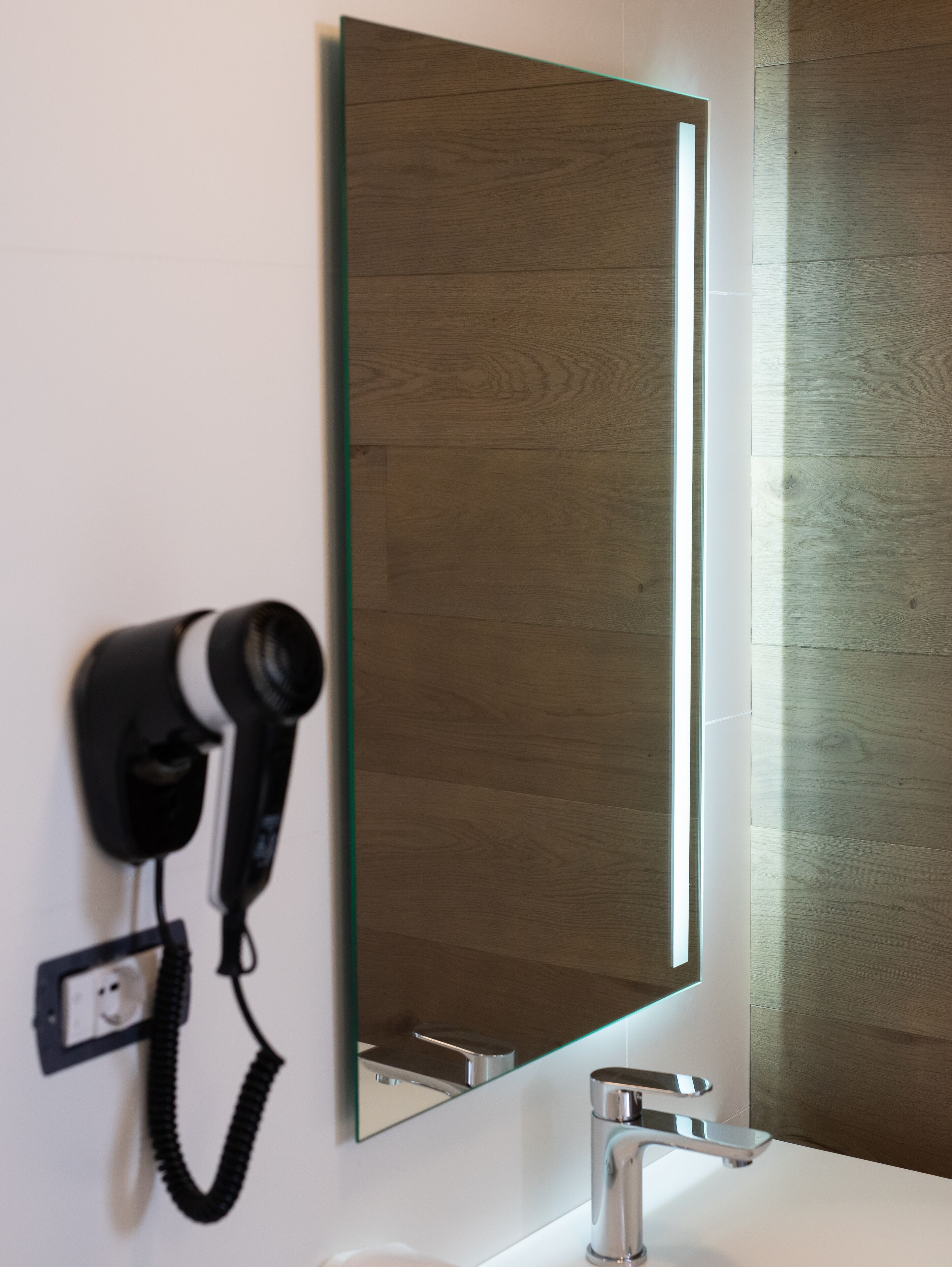 A bathroom with a hairdryer mounted on the wall, a large mirror, and a modern sink.