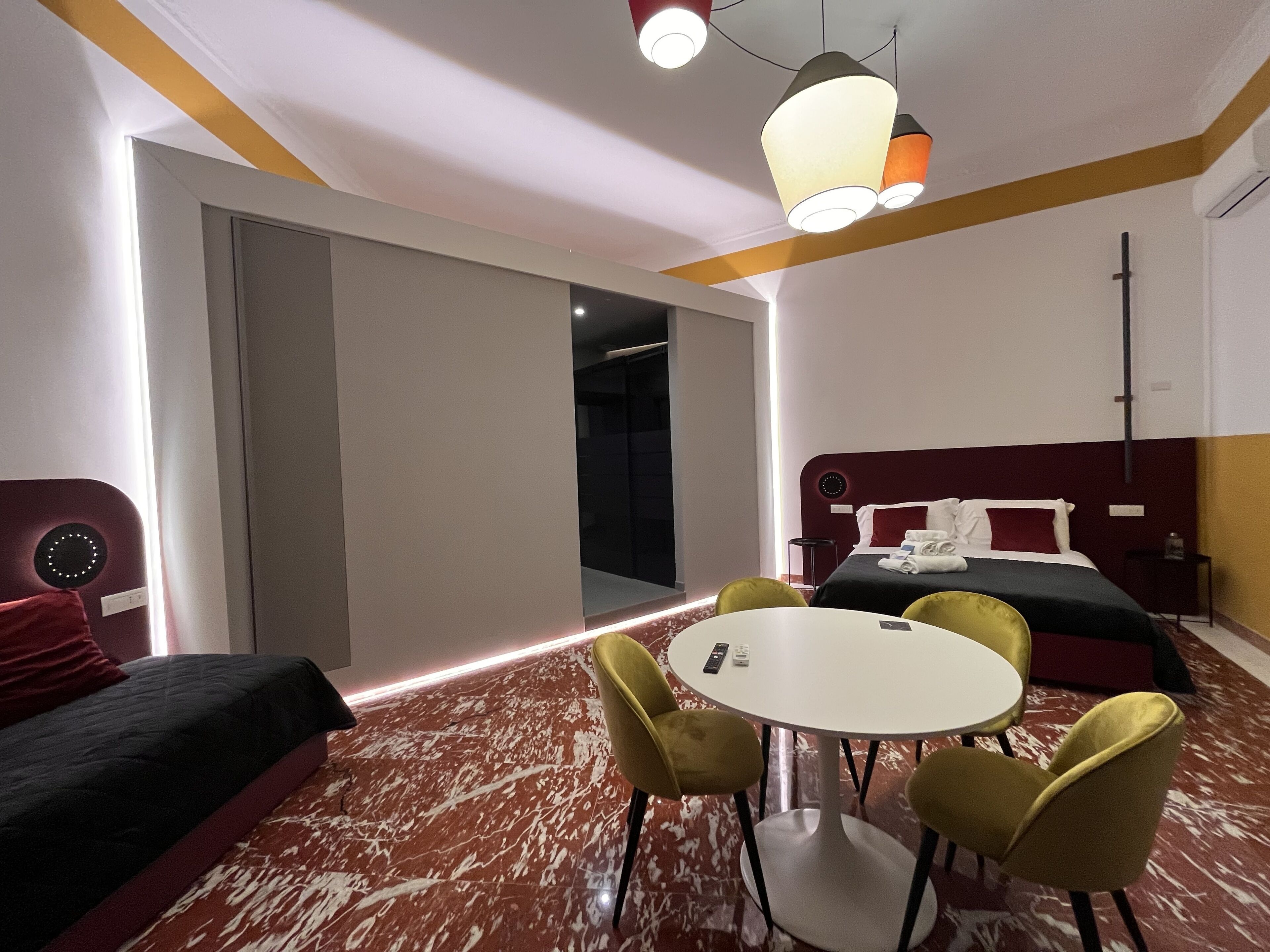 Ein modernes Hotelzimmer mit einem Bett, einem runden Tisch mit Stühlen, einem kleinen Tisch mit Telefon und einer roten Akzentwand.