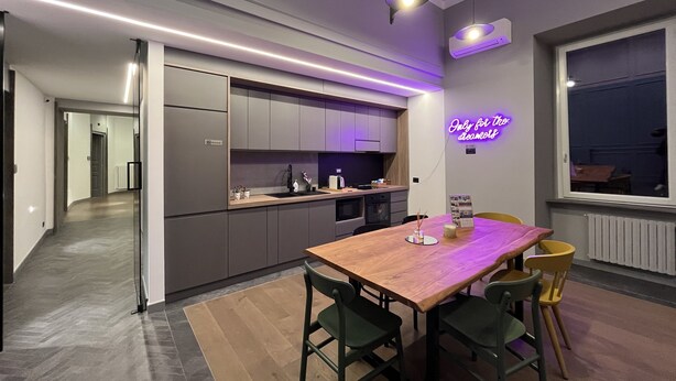 A modern kitchen with grey cabinets, a wooden dining table with chairs, and a neon sign on the wall. - Rettifilo 311 (Naples)