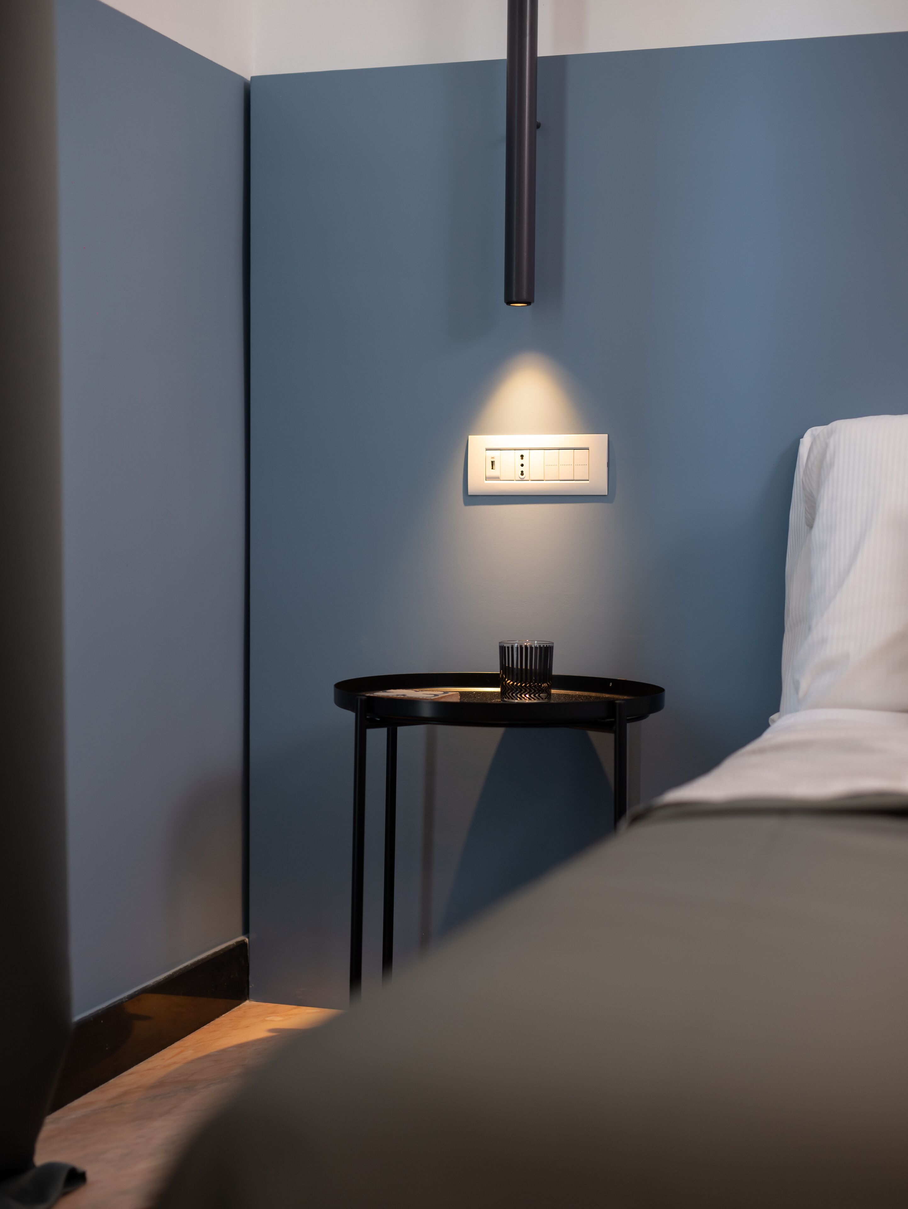 Une chambre d’hôtel avec un lit, une table de chevet avec une lampe et une prise de courant fixée au mur.
