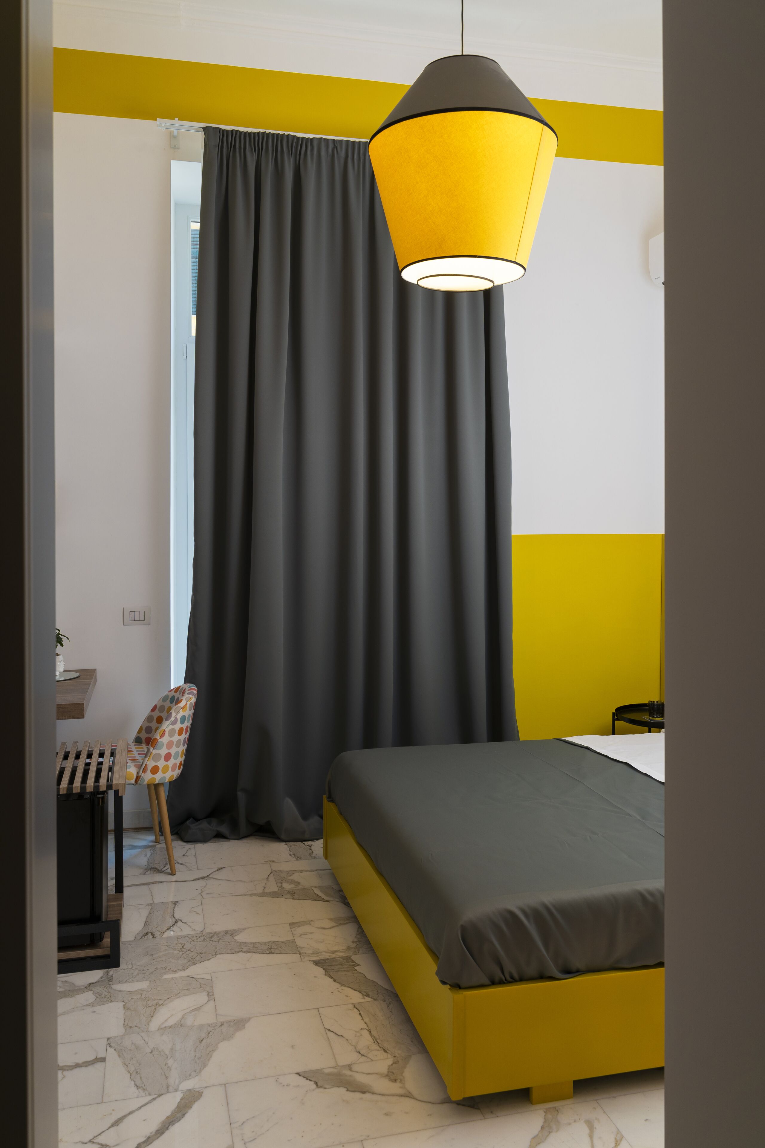 Ein Schlafzimmer mit einem Bett, einem Sessel, einem Schreibtisch und einem Fenster mit Vorhängen.