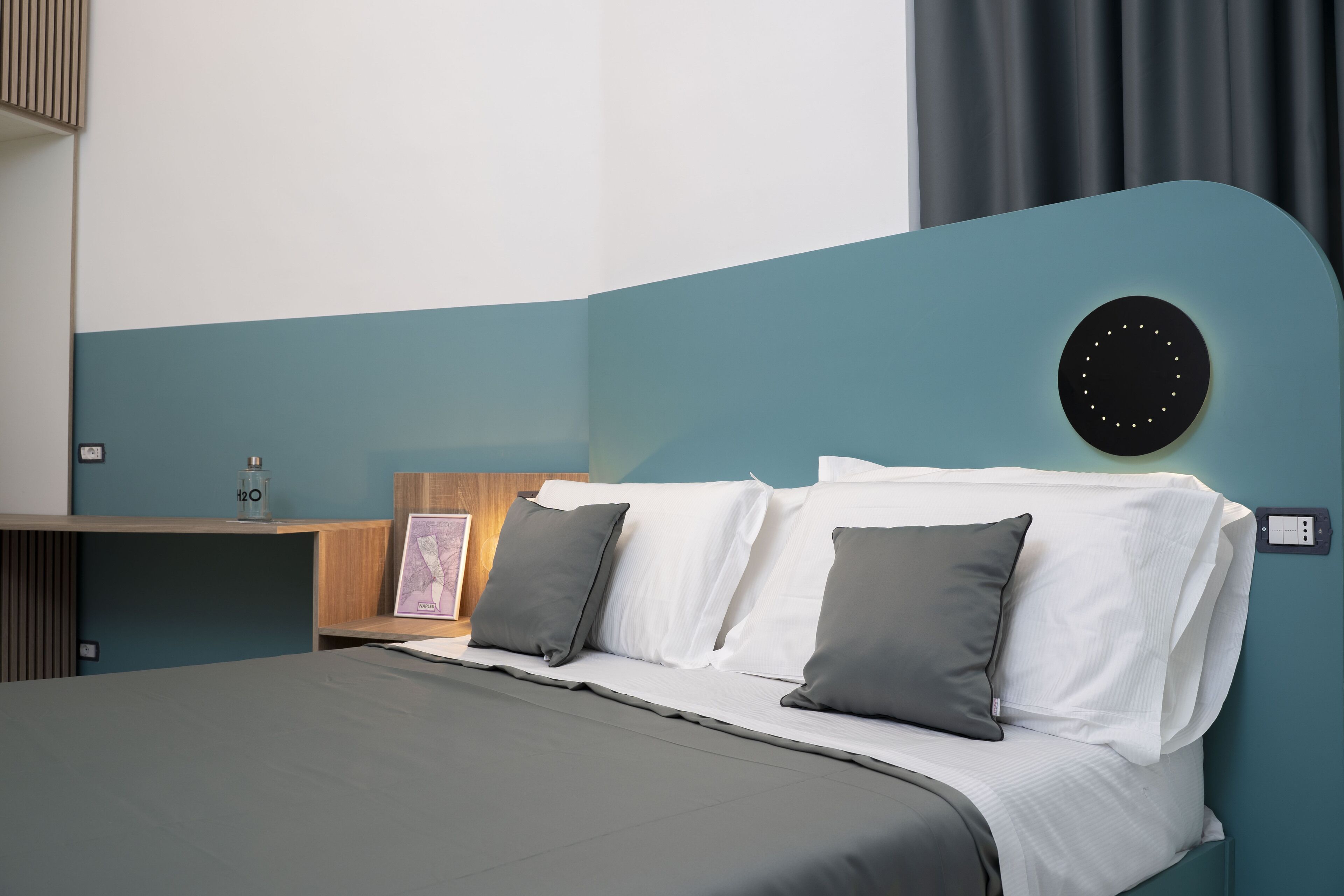 Une chambre à coucher moderne avec une tête de lit incurvée, une table de chevet avec une lampe et un panneau de commande fixé au mur.