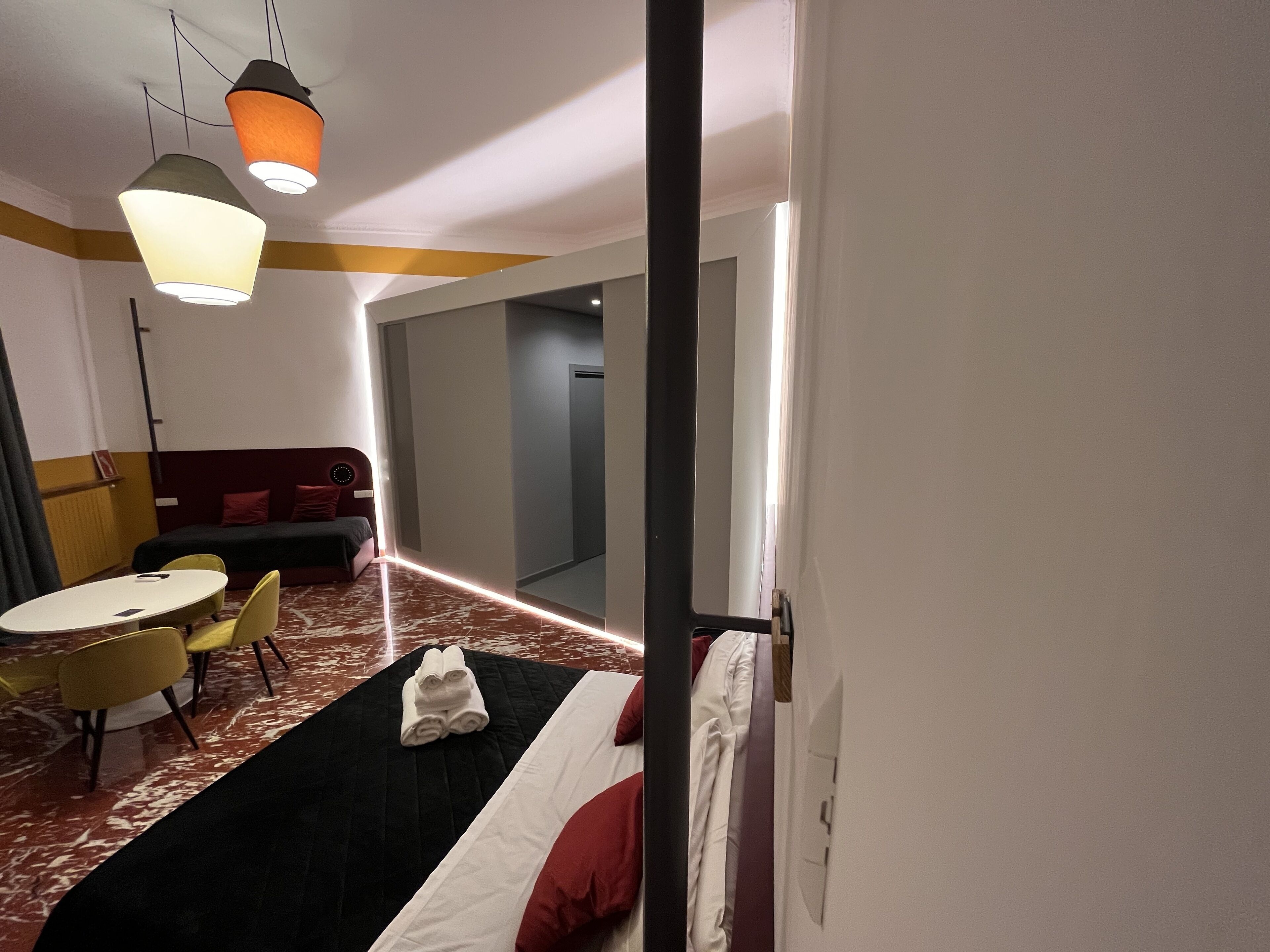 A hotel room with a bed, a desk with chairs, a sofa, and pendant lights.