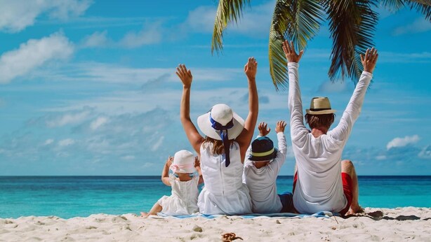 En familj på fyra personer på en sandstrand med en klarblå himmel och havet i bakgrunden.