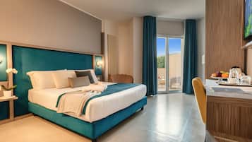 Habitación de hotel con cama, escritorio con silla, mesa de comedor con sillas, planta en maceta y vista al exterior.
