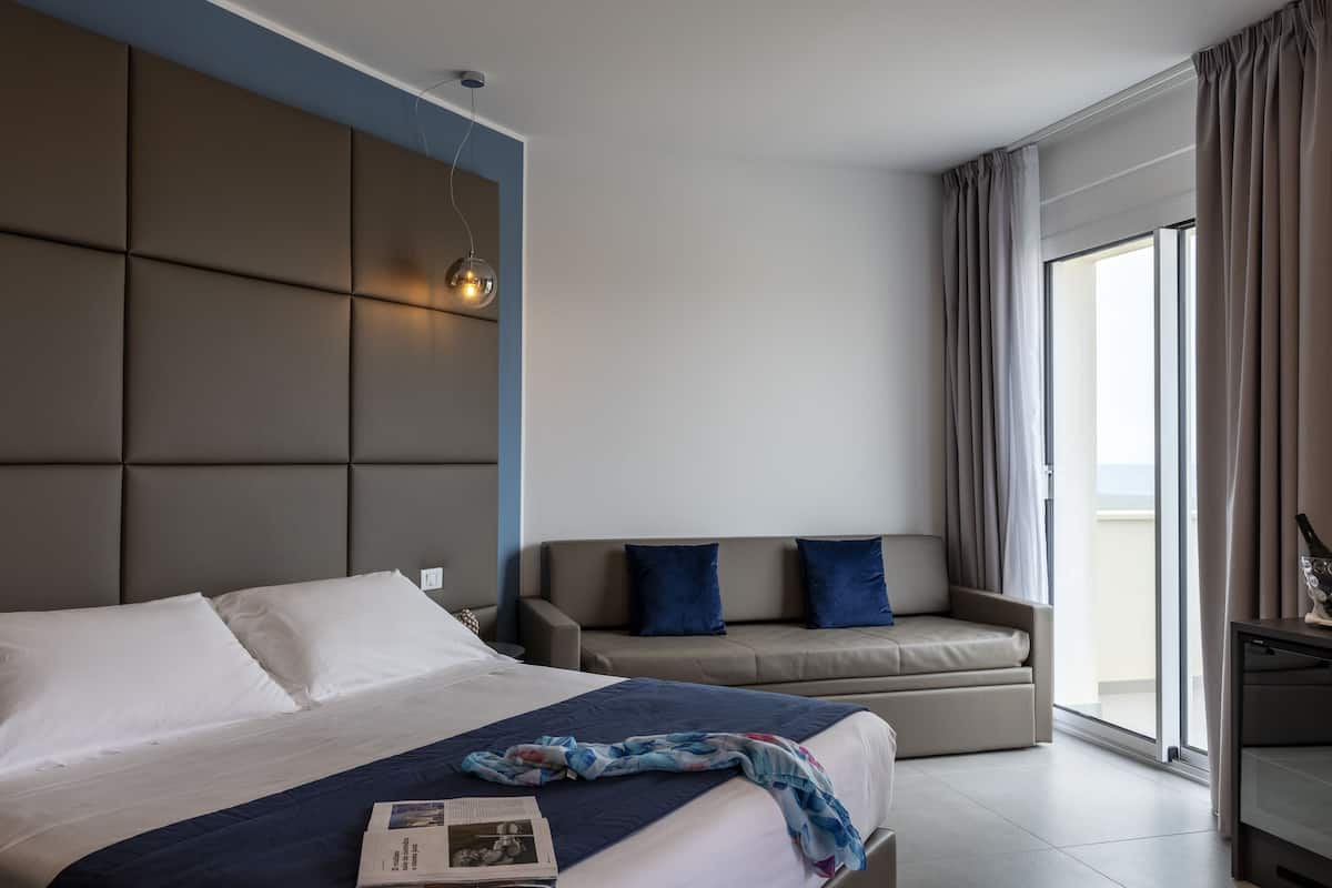 Ein modernes Hotelzimmer mit einem großen Bett, einer Sitzecke und einem Balkon mit Vorhängen.