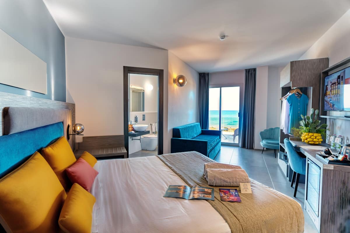 Ein modernes Hotelzimmer mit einem großen Bett, einem Schreibtisch, einem Fernseher und Meerblick.