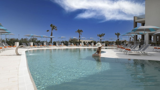 A pool area with lounge chairs and umbrellas, palm trees, and a clear sky. - Resort La battigia Beach And Spa (Alcamo)