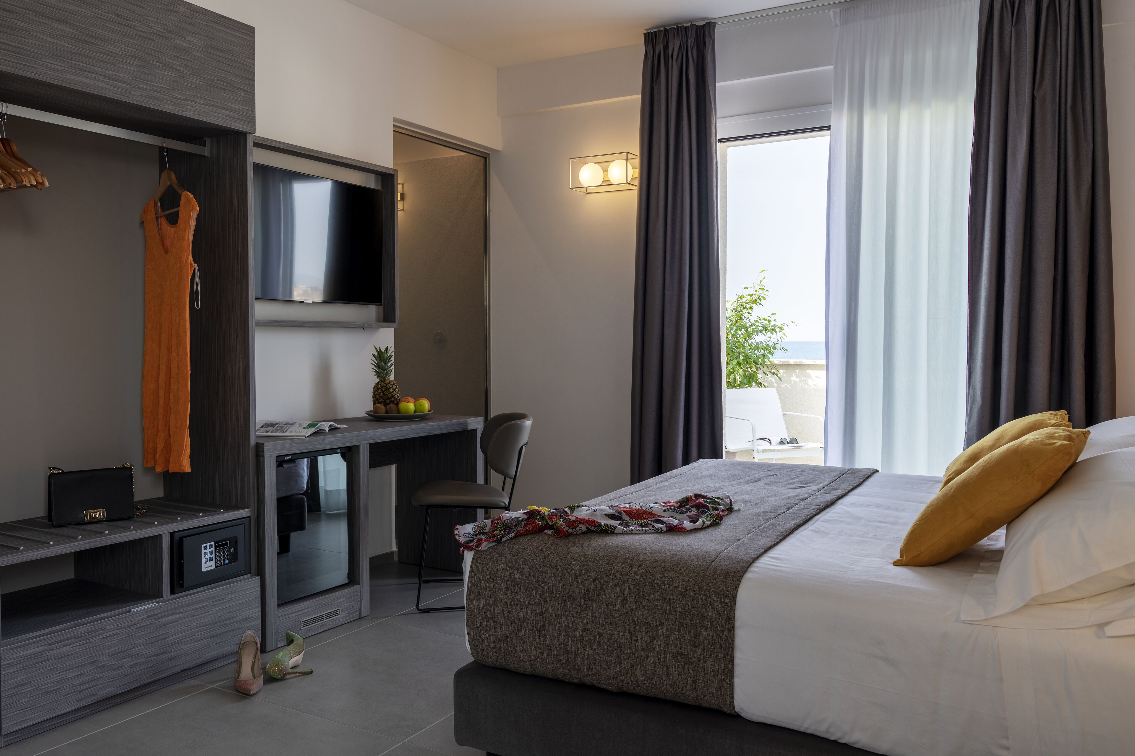 A modern hotel room with a bed, a desk, a TV, and a view of the outdoors.