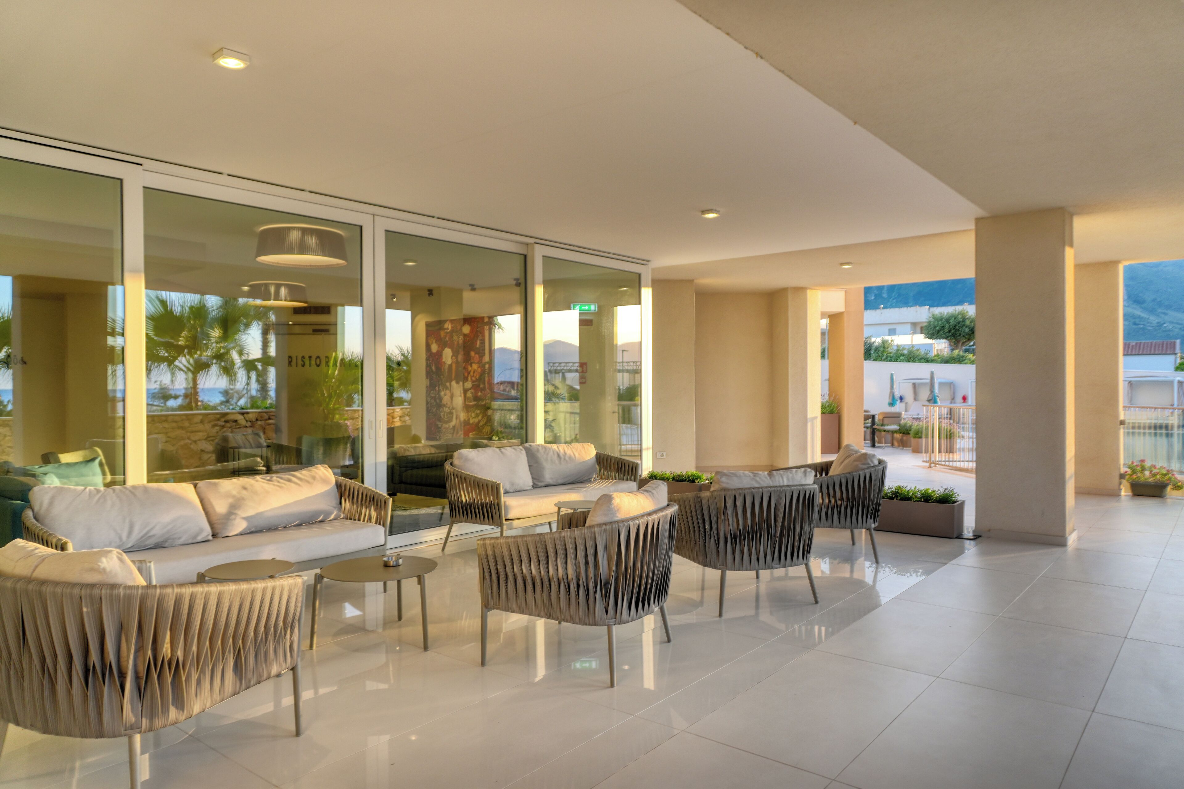 Un patio interior moderno con espacios de descanso, amplias puertas de cristal y vistas al exterior.