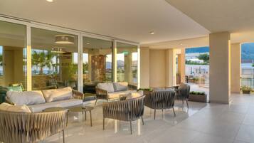 Un patio interior moderno con espacios de descanso, amplias puertas de cristal y vistas al exterior.