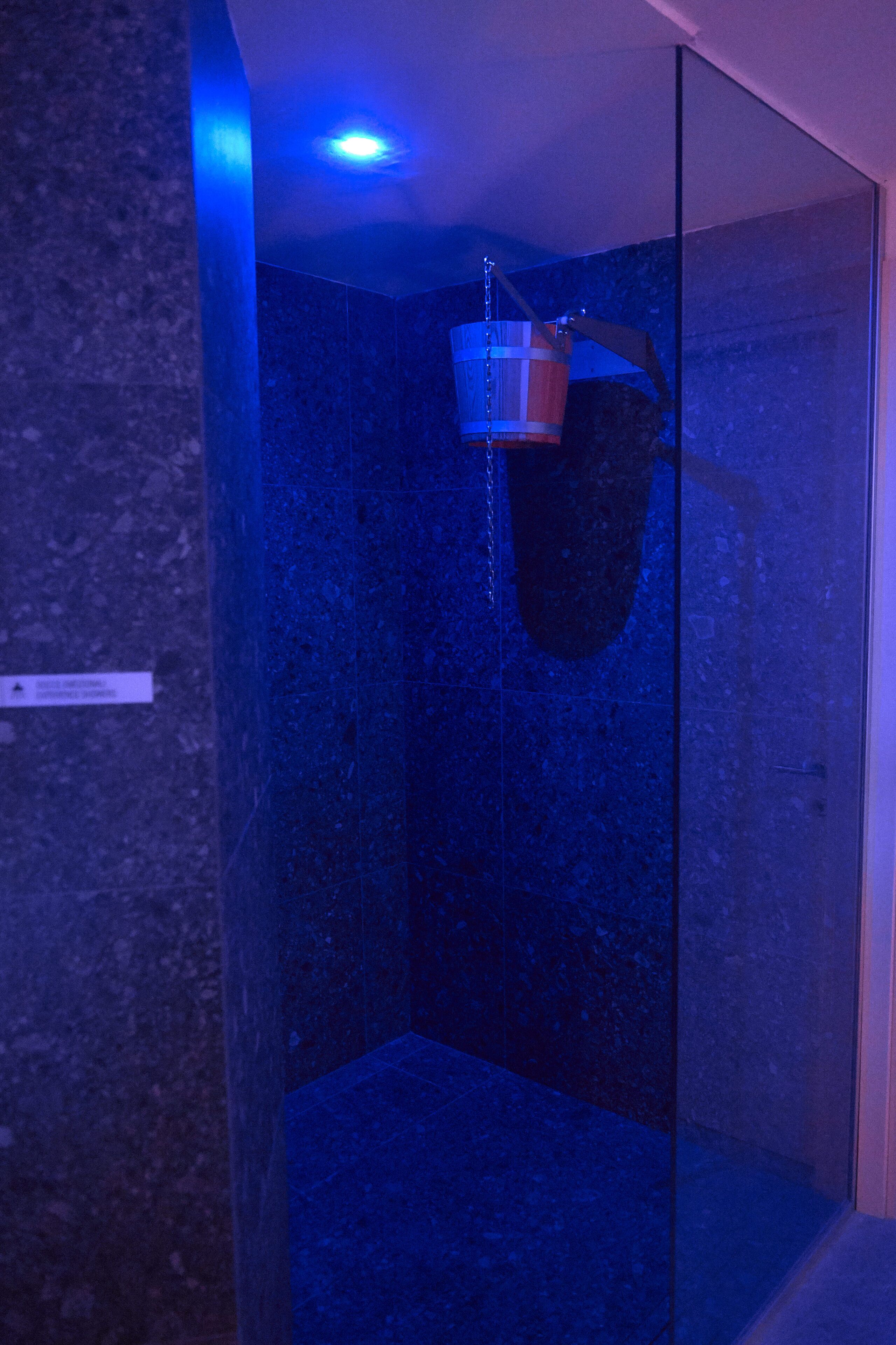 A modern bathroom with a glass shower enclosure, a visible water spout, and a ceiling light.