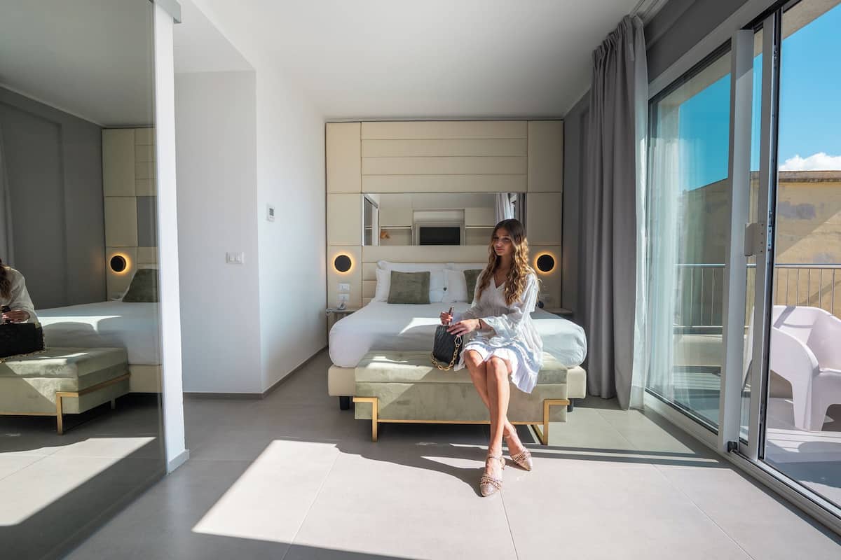 Ein modernes Hotelzimmer mit einem großen Bett, einer separaten Sitzecke und einem Balkon mit Blick.