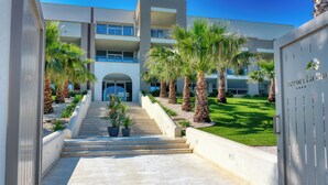 A modern hotel entrance with a staircase leading to the main building, surrounded by palm trees and a well-maintained lawn. - Resort La battigia Beach And Spa (Alcamo)