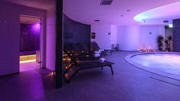 Area piscina interna moderna con poltrona relax e piscina riscaldata, caratterizzata da un soffitto curvo e illuminazione d'ambiente.