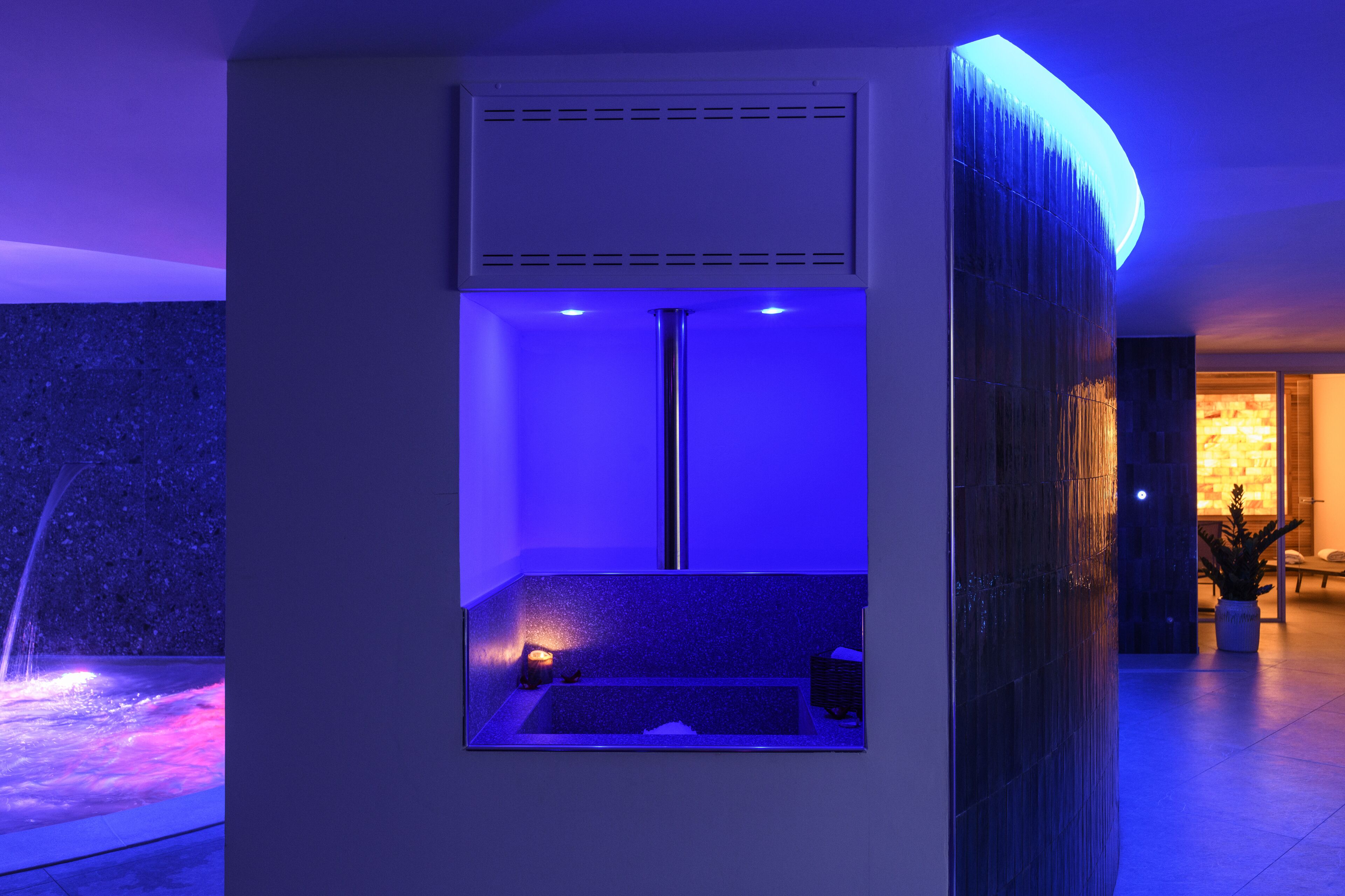 A modern spa room with a blue-lit tub, a ventilation system, and a stone wall.
