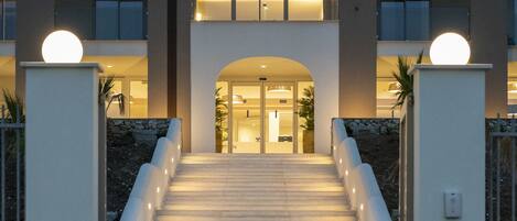 A modern building with a central entrance, a staircase leading up to the entrance, and two spherical lights on either side of the staircase.