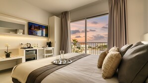 A modern hotel room with a large bed, a desk with a computer, a TV, and a balcony with a sunset view. - Resort La battigia Beach And Spa (Alcamo)