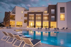 Un hotel moderno con piscina, sillas de descanso y espacios interiores bien iluminados.