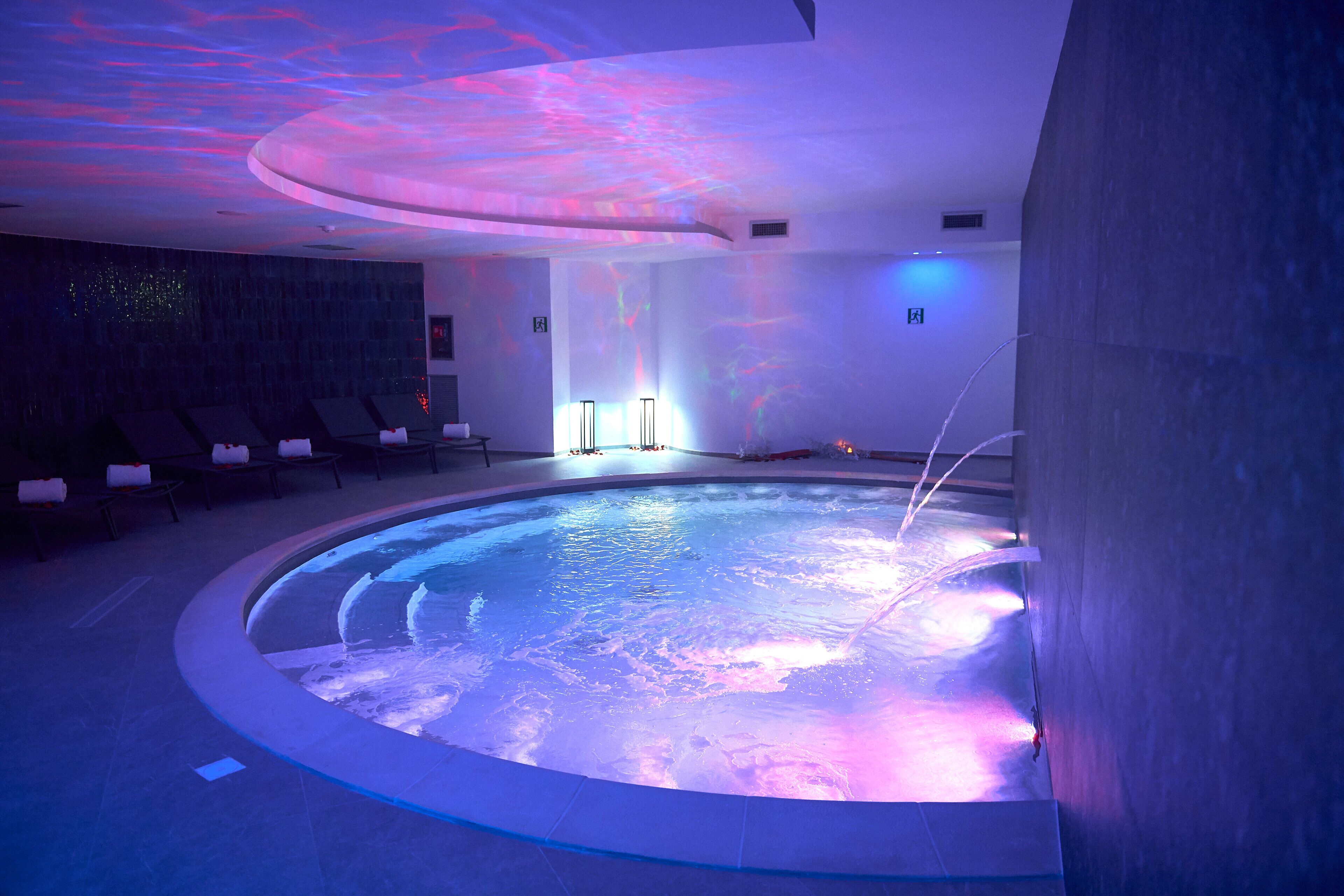 A modern indoor pool with a circular design, ambient lighting, and a ceiling projection.