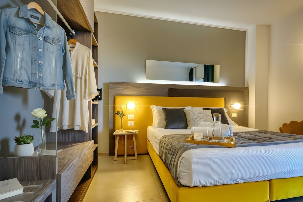Ein modernes Hotelzimmer mit Bett, Nachttischen, einem Spiegel und einem Kleiderschrank.