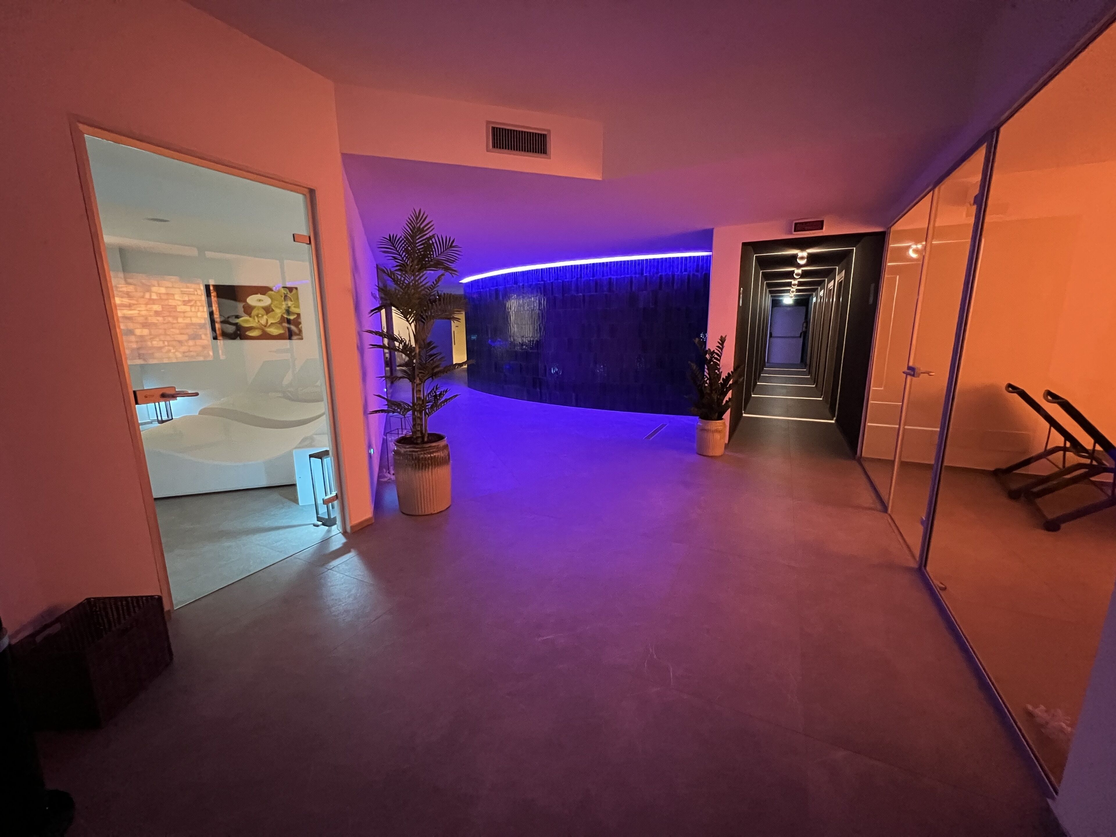 Um interior moderno com uma área de recepção, um corredor com parede iluminada em azul e uma escadaria.
