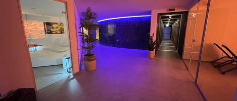 Um interior moderno com uma área de recepção, um corredor com parede iluminada em azul e uma escadaria.