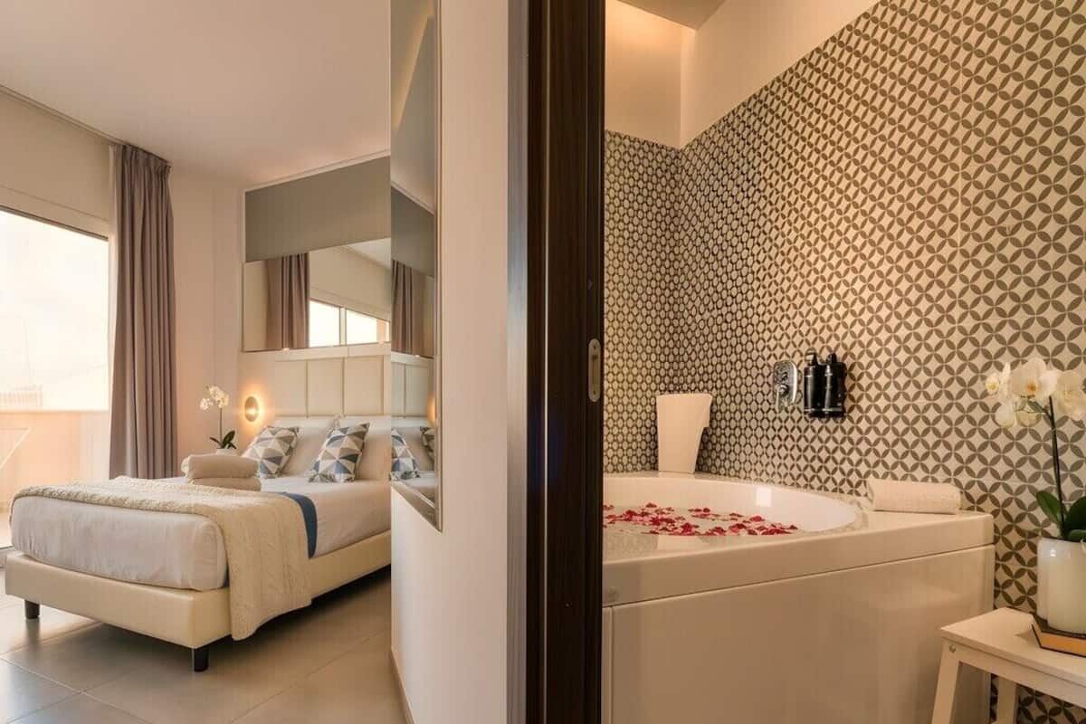Ein modernes Hotelzimmer mit einem großen Bett, einem separaten Badezimmer mit einem gemusterten Wandbild und einem kleinen Tisch mit einer Blumenvase.