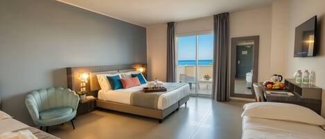 A hotel room with a bed, a chair, a desk, and a view of the sea.