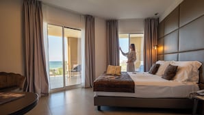 A hotel room with a large bed, a sofa, a balcony with a view of the sea, and a sliding glass door. - Resort La battigia Beach And Spa (Alcamo)