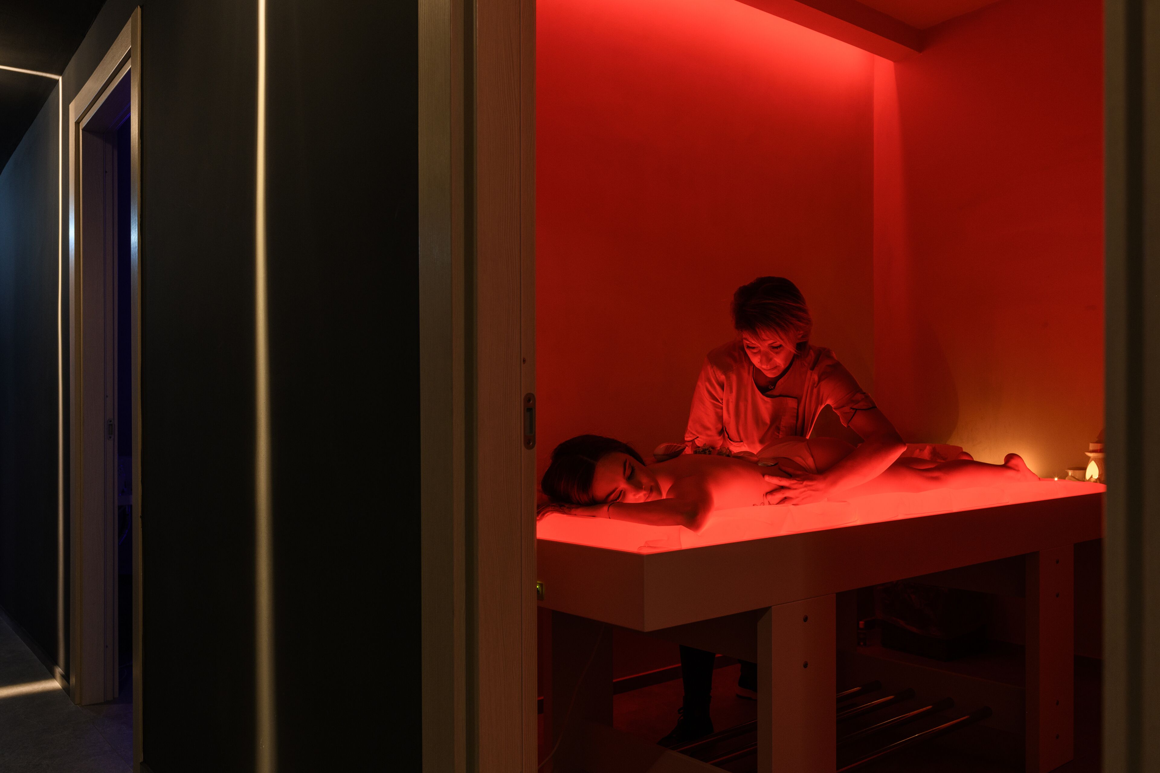 Une pièce avec une table de massage éclairée de lumière rouge, sur laquelle est allongée une personne.
