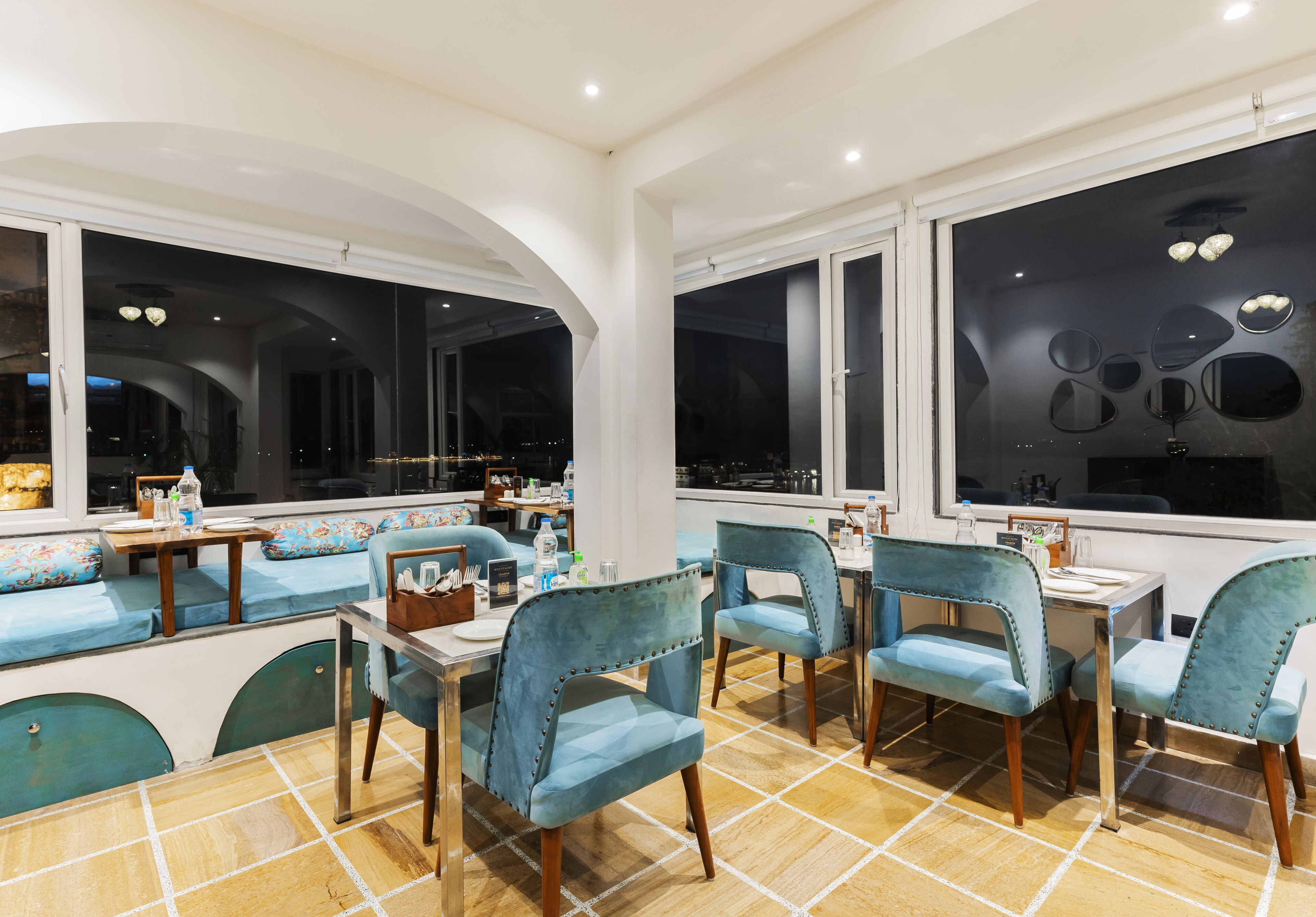 A restaurant with blue upholstered chairs, wooden tables, and large windows offering views of the city.