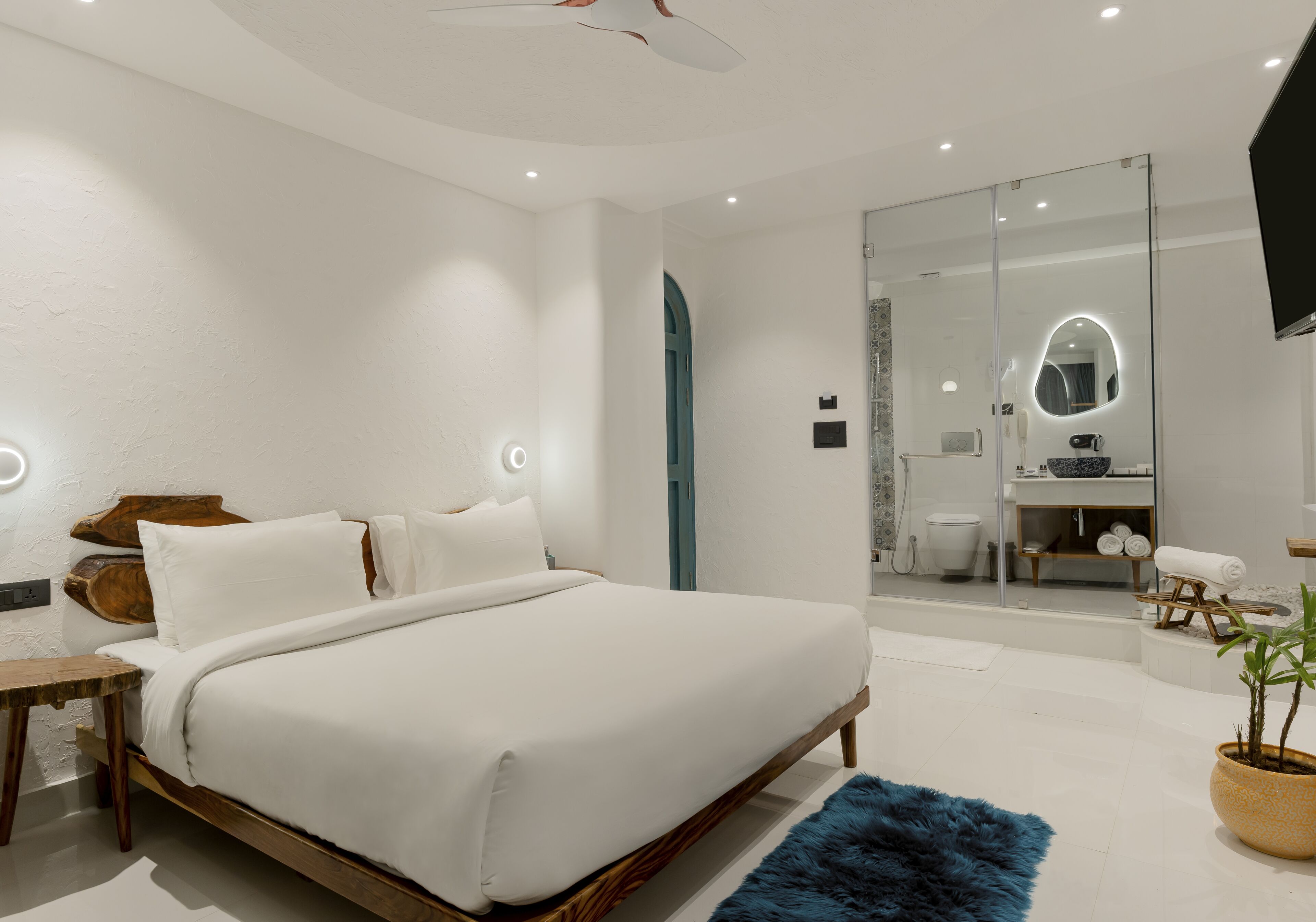Een moderne slaapkamer met een groot bed, nachtkastjes, een spiegel en een badkamer zichtbaar door een glazen deur.