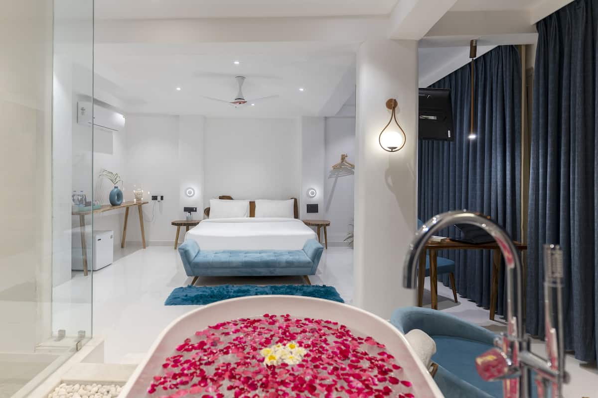 A modern bedroom with a large bed, a bathtub filled with rose petals, and a vanity with a mirror.