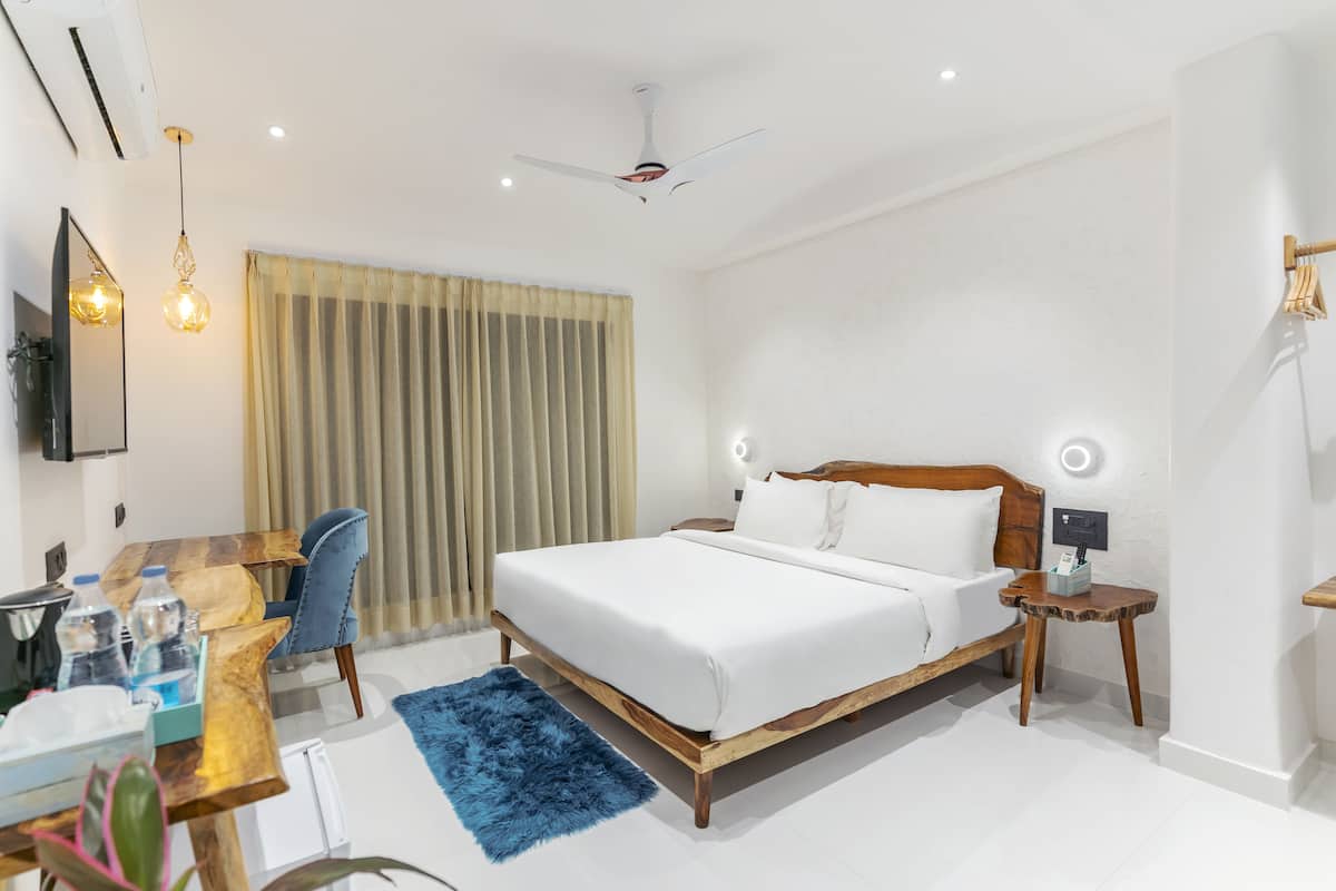 A modern hotel room with a wooden bed, a desk with a chair, a blue rug, and a ceiling fan.