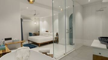 Ein modernes Schlafzimmer mit einem großen Bett, einer Duschkabine aus Glas, einer Badewanne und einem Nachttisch mit einer Wasserflasche.