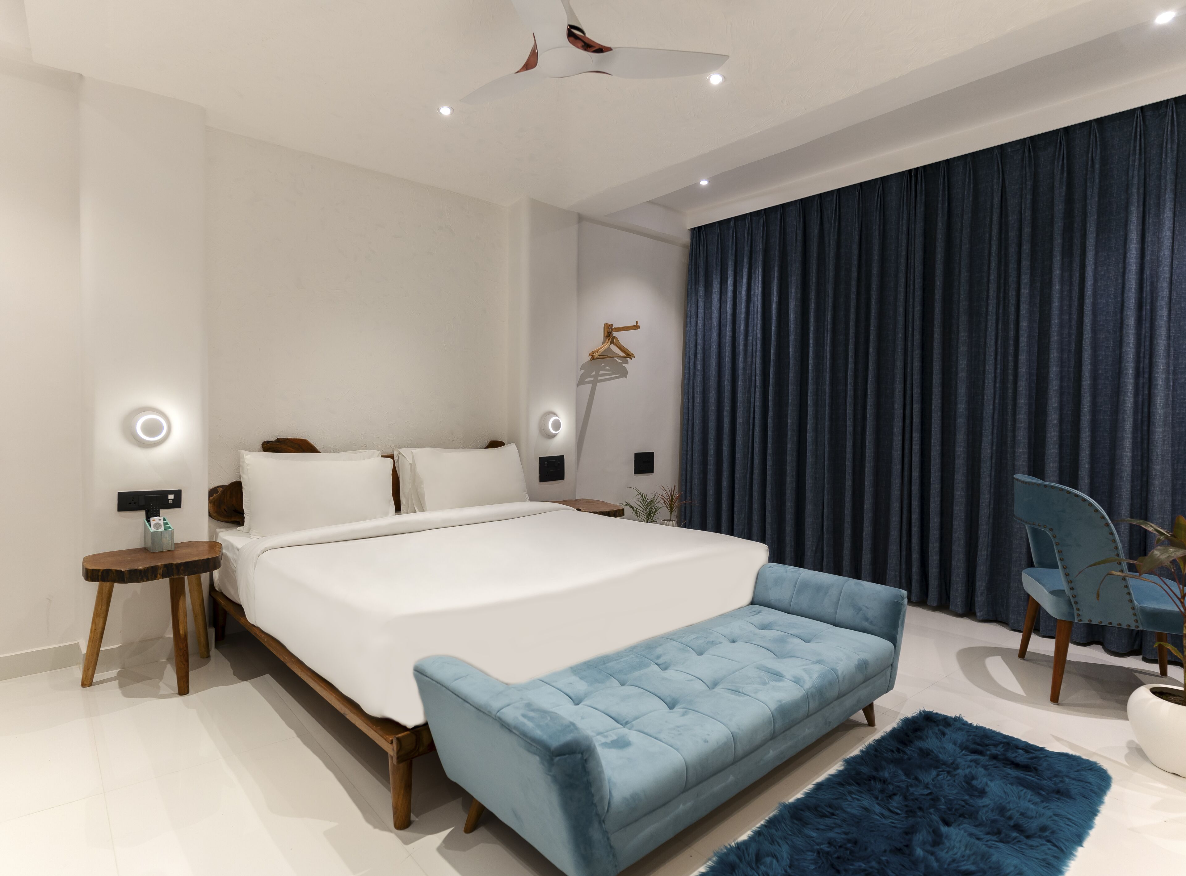 Ein modernes Schlafzimmer mit einem großen Bett, Nachttischen, einem Deckenventilator und einem dunklen Vorhang.
