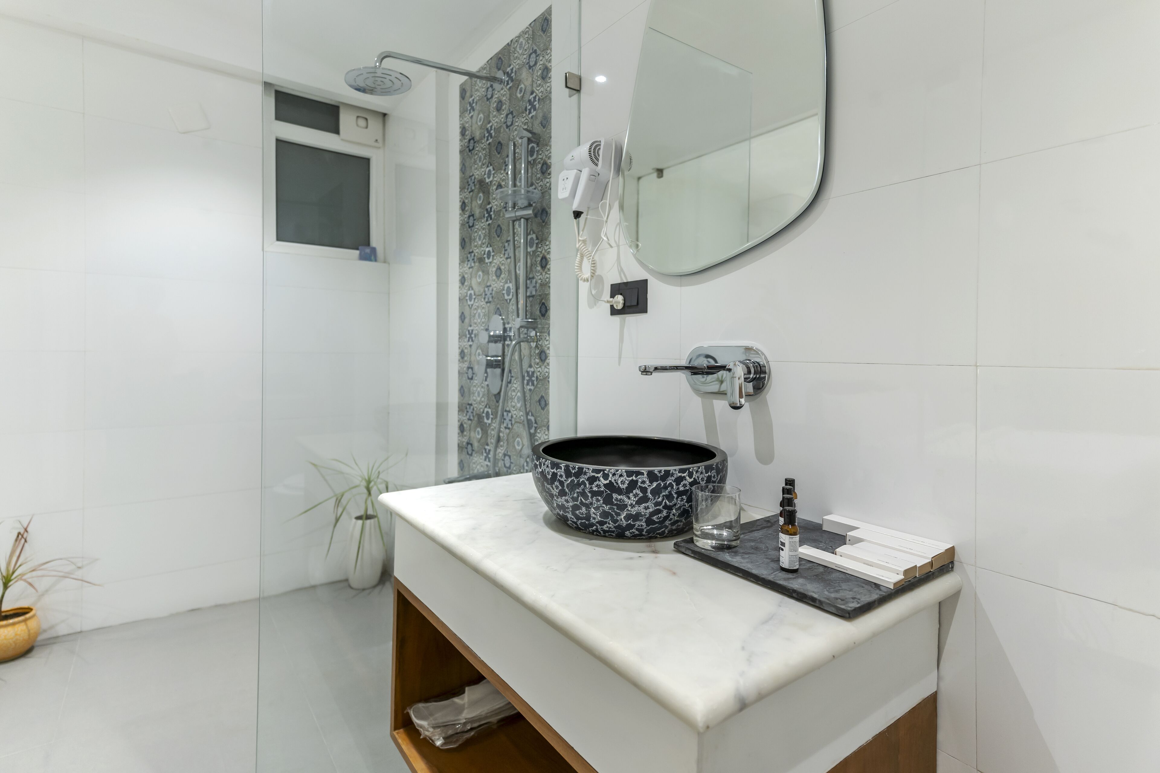 Une salle de bain moderne avec un meuble-lavabo blanc, un grand miroir et un lavabo sur colonne aux motifs noir et blanc.