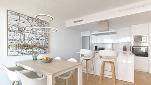 Een moderne keuken met witte kasten, een eethoek met een houten tafel en witte stoelen, en een groot abstract kunstwerk aan de muur.