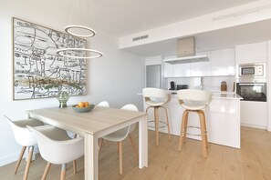 A modern kitchen with white cabinetry, a dining area with a wooden table and white chairs, and a large abstract artwork on the wall.