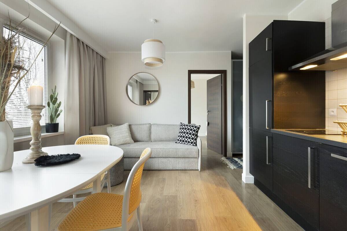 Cocina moderna con armarios oscuros, un espejo redondo y un comedor con mesa blanca y sillas de mimbre.