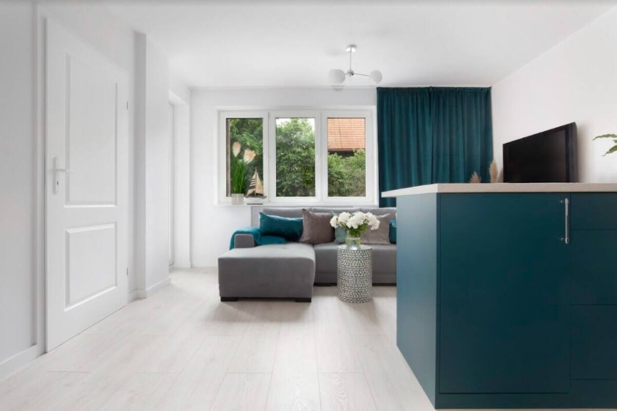 Una sala de estar moderna con un sofá gris, cortinas color turquesa y un televisor sobre un mueble.