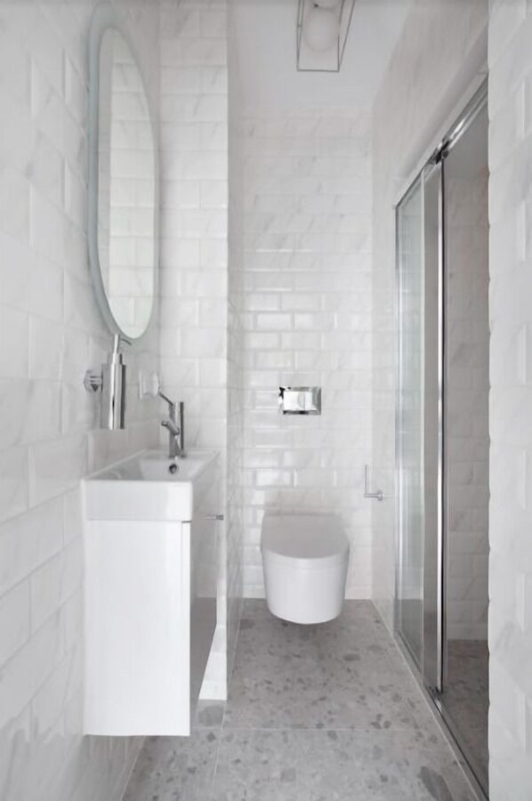 Un baño moderno con azulejos blancos tipo metro, cabina de ducha con vidrio y lavamanos pedestal blanco.